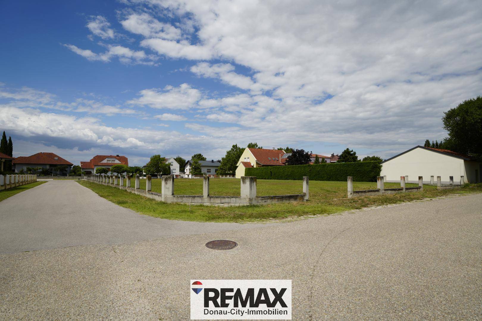 Weitläufiges grünes Grundstück mit niedriger Betonmauer und Blick auf die umliegende Wohnbebauung.