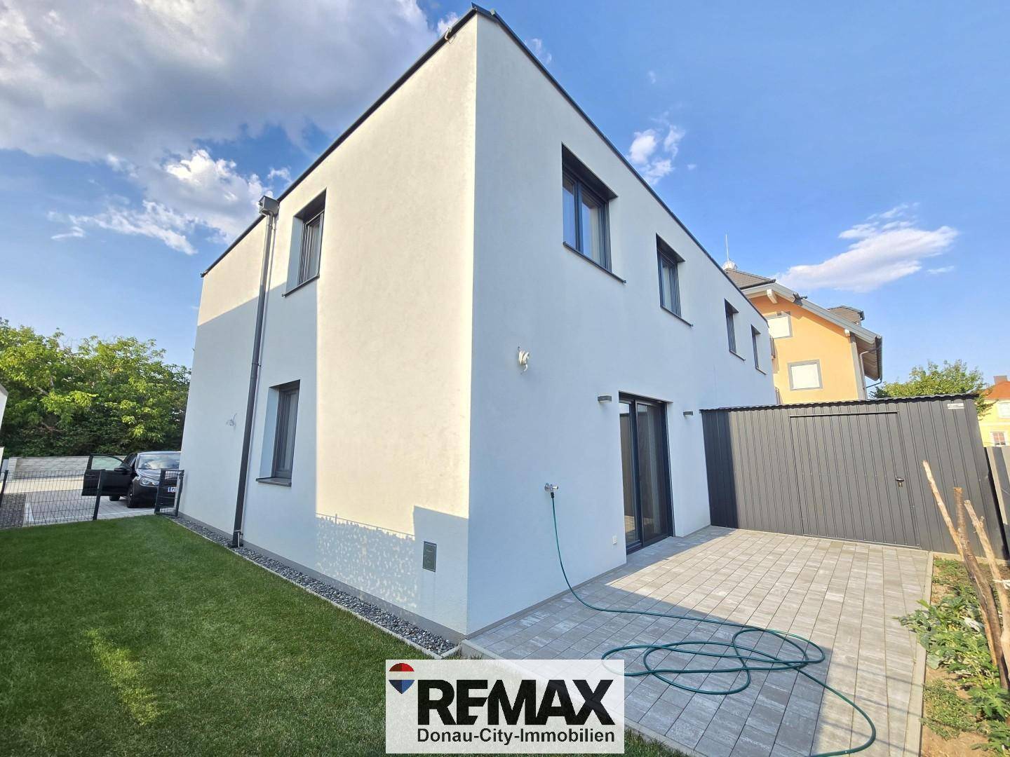 Rückseite eines modernen Reihenhauses mit kleiner Terrasse, Rasenfläche und Schiebetüren.