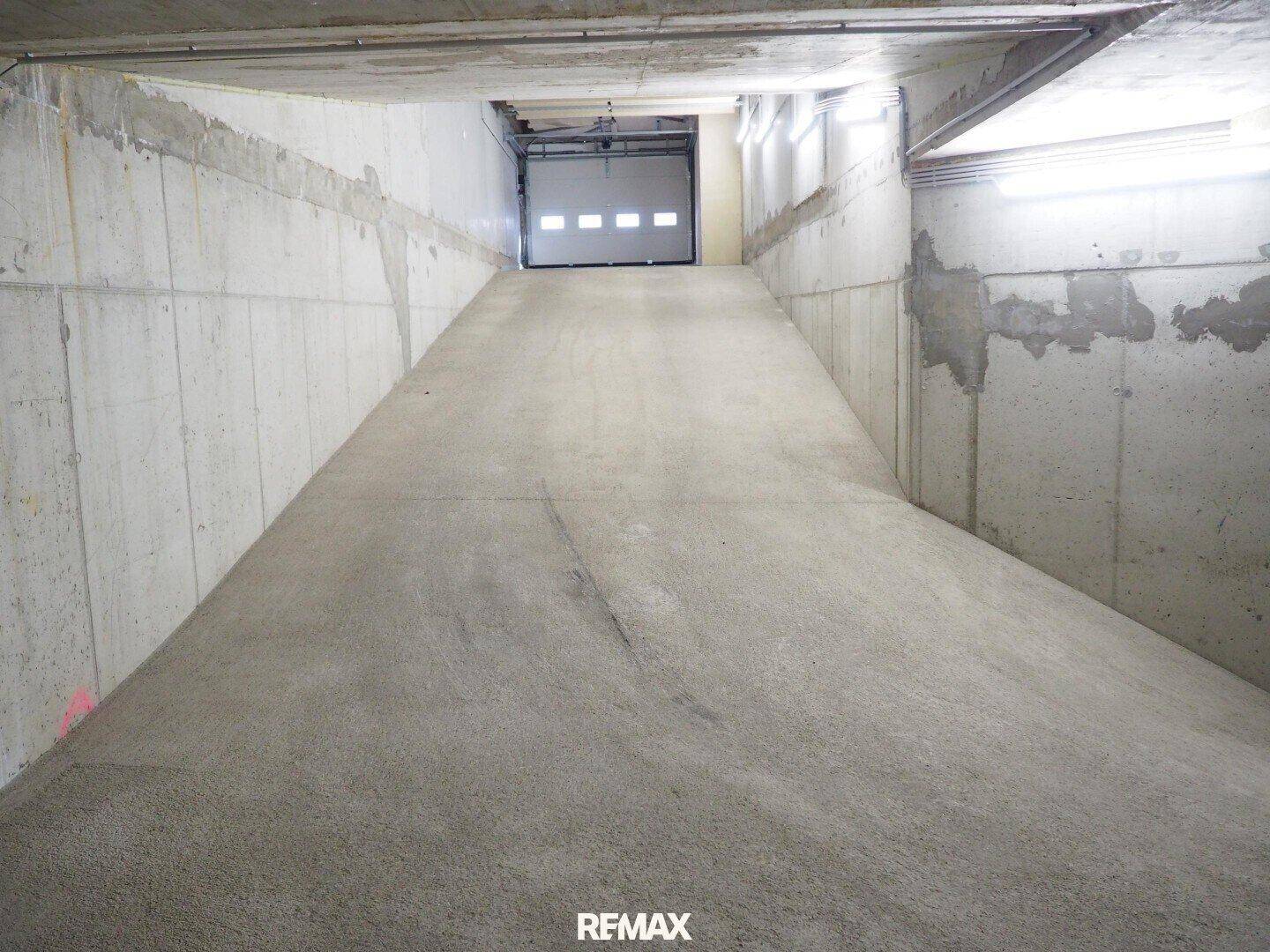 Betonrampe führt zur Garagenausfahrt, umgeben von robusten Betonwänden und einer Decke.