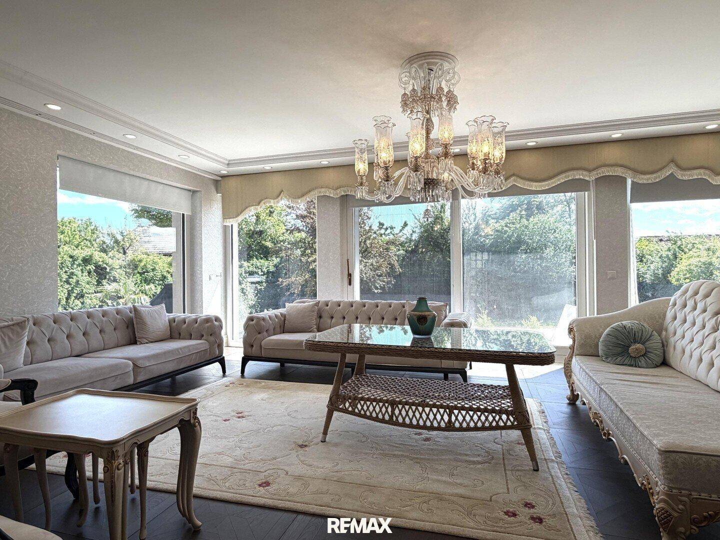 Helles Wohnzimmer mit großen Fenstern, bequemen Sofas und elegantem Kronleuchter.