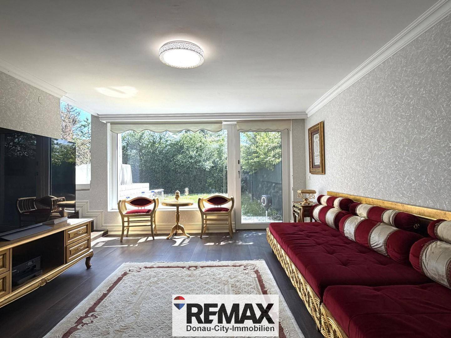 Gemütliches Wohnzimmer mit rotem Sofa, Fernseher und Blick in den Garten.