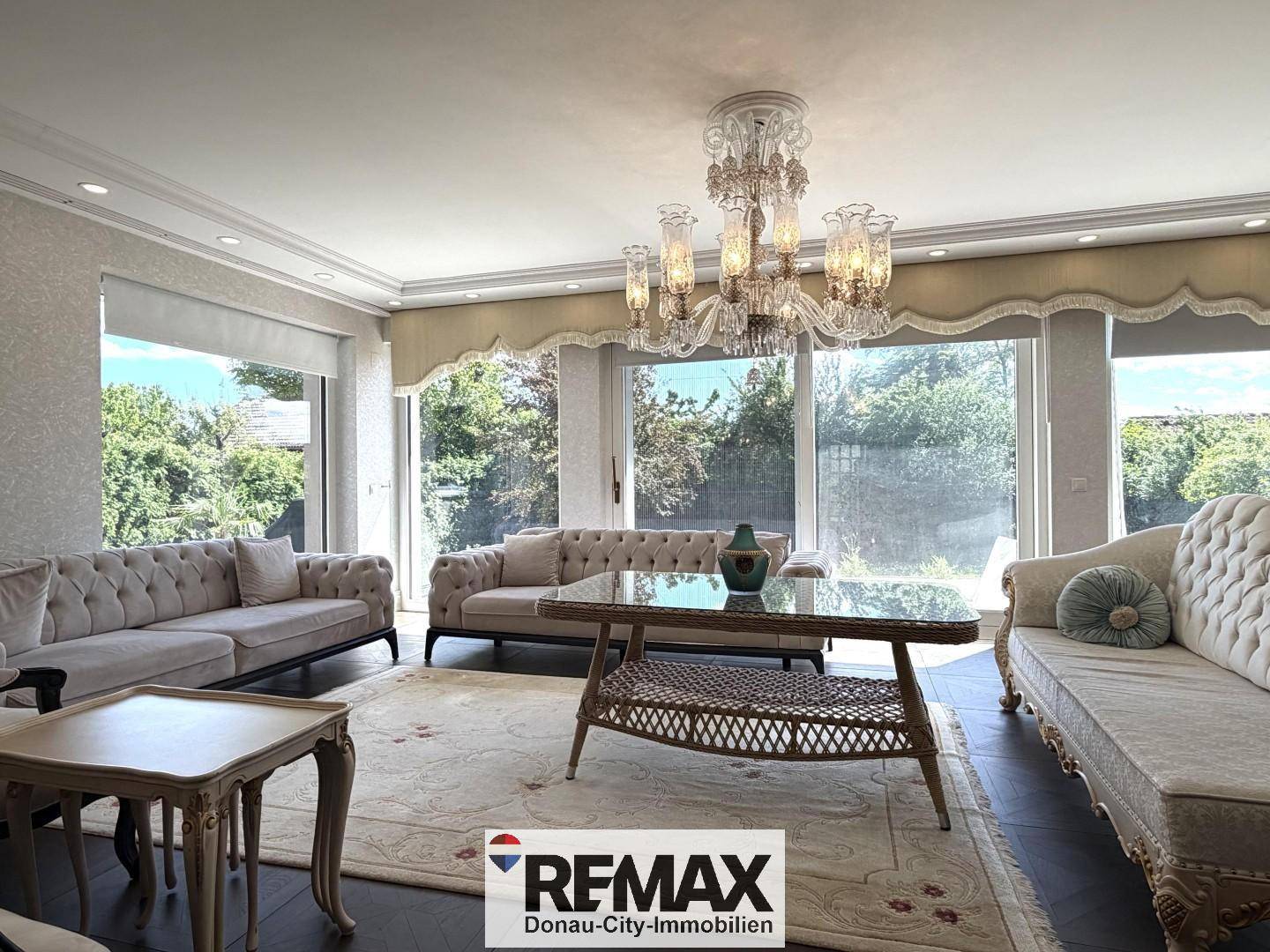 Helles Wohnzimmer mit großen Fenstern, eleganten Sofas und Blick ins Grüne.