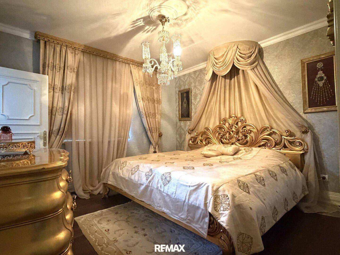 Luxuriöses Schlafzimmer mit Himmelbett, goldenen Möbeln und elegantem Kronleuchter.