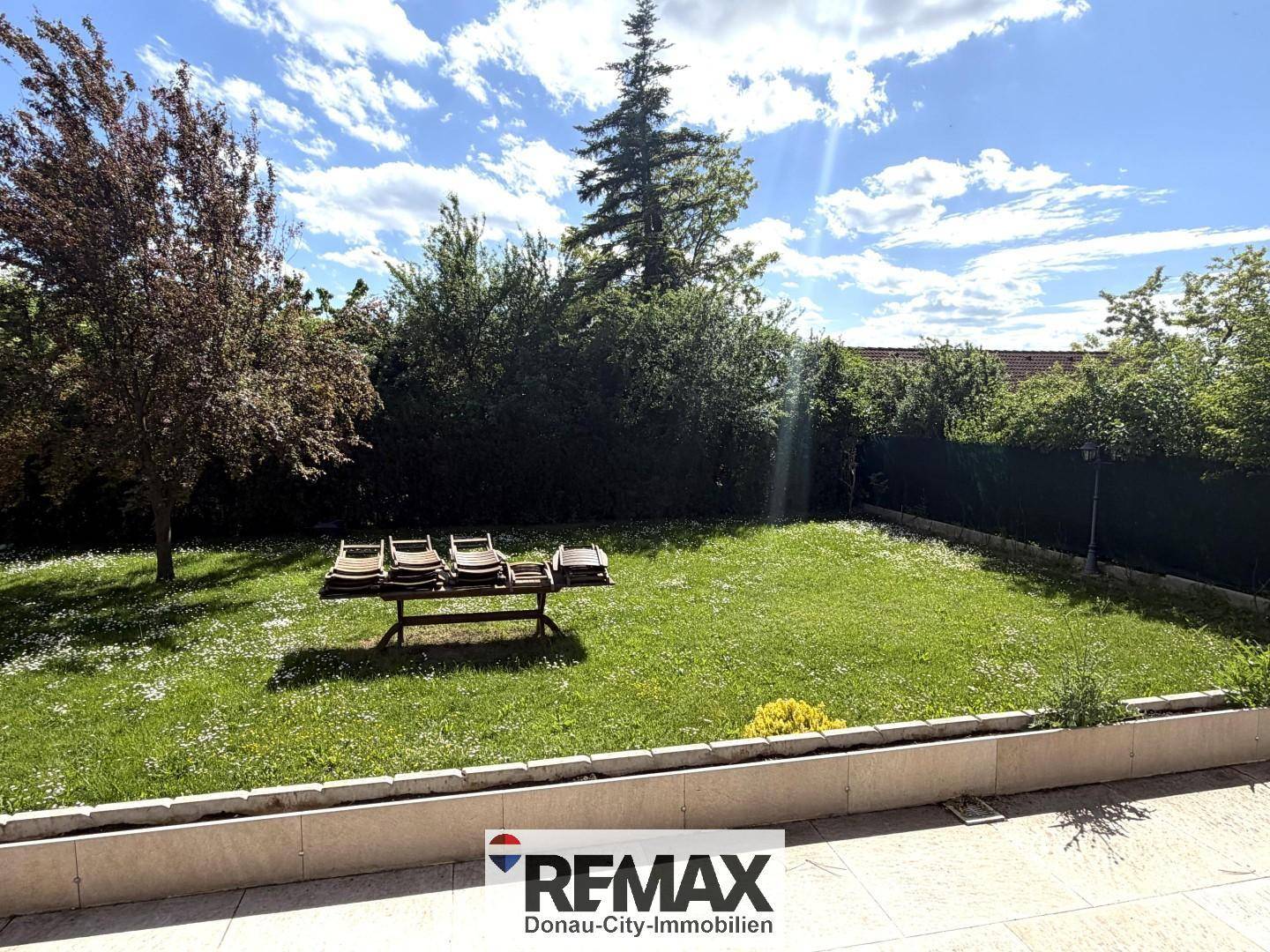 Großer, gepflegter Garten mit Rasenfläche, Bäumen und Liegestühlen.