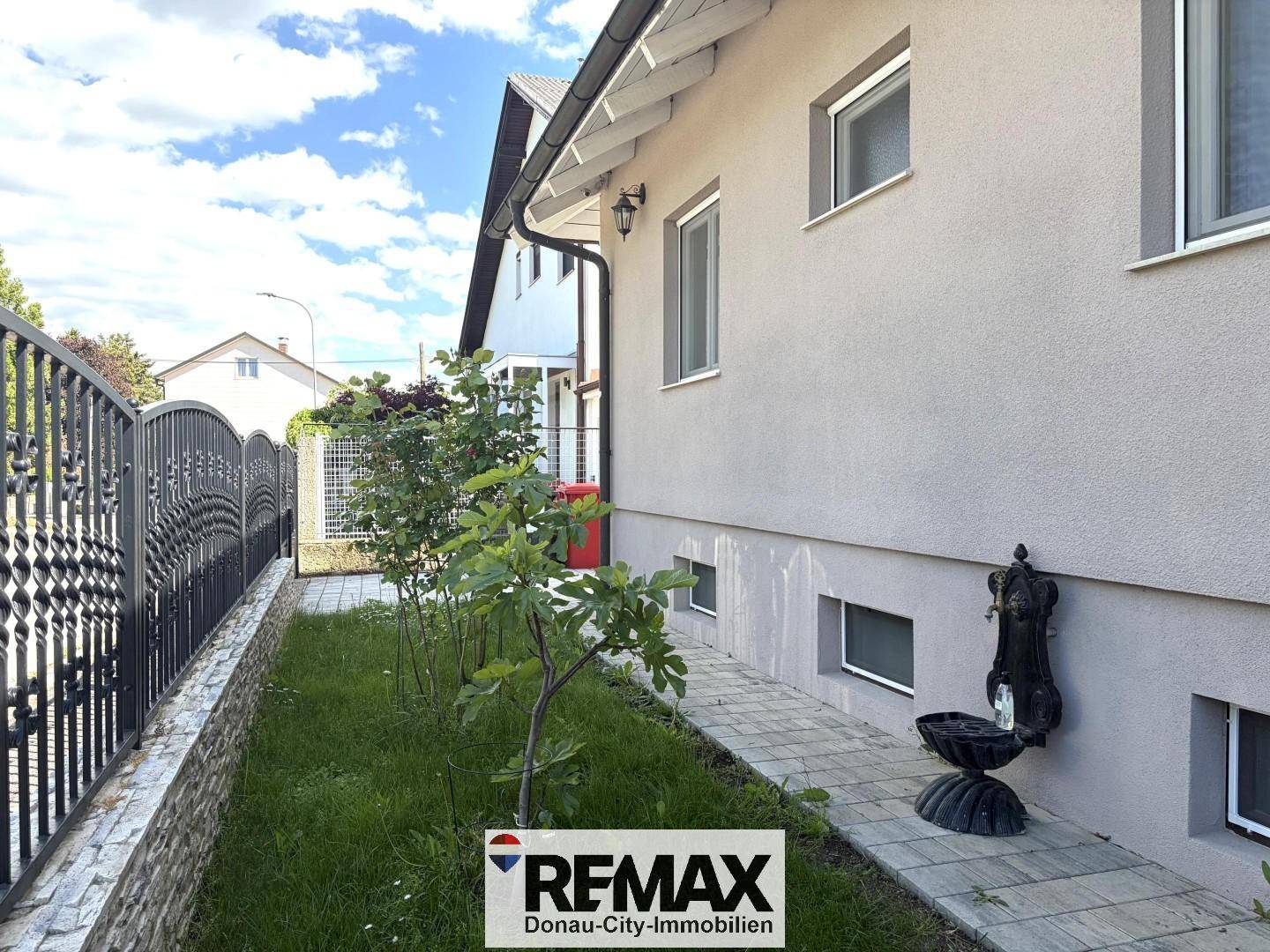 Seitenansicht des Hauses mit gepflastertem Weg und dekorativem Brunnen.