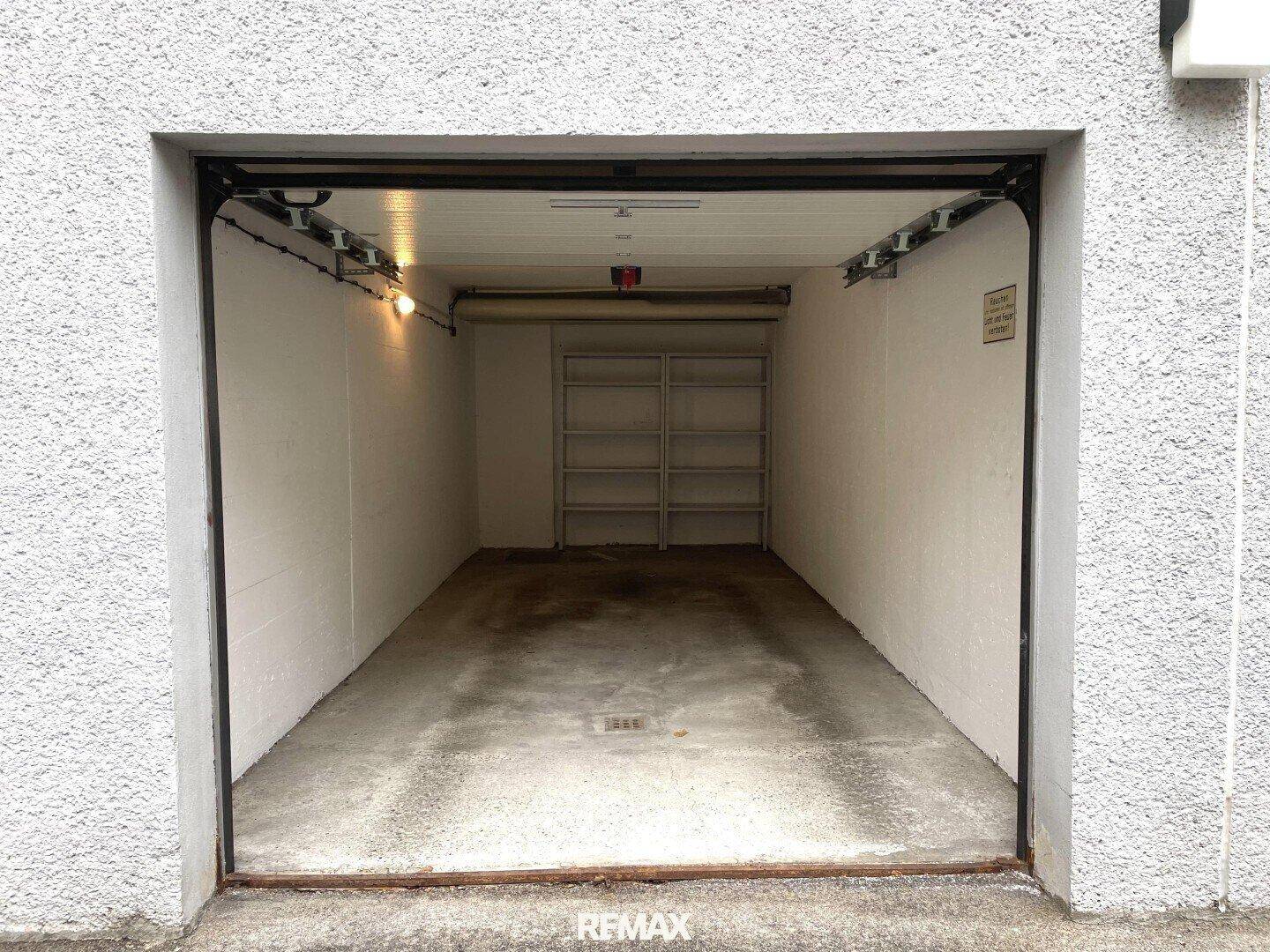 Einzelgarage mit offenem Tor, Betonboden und Regalen für zusätzlichen Stauraum, praktisch und geräumig.