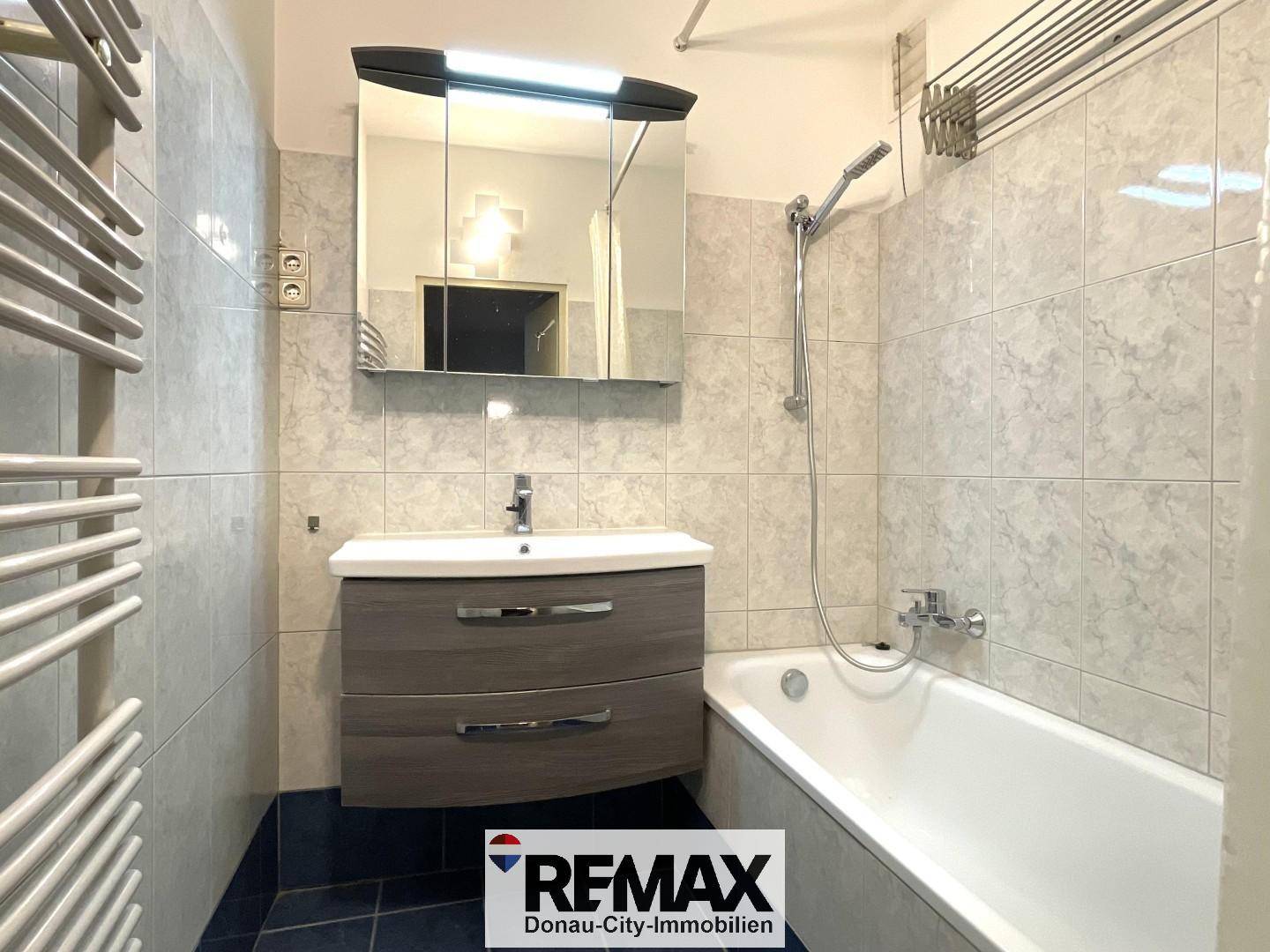 Funktionales Badezimmer mit Badewanne, Waschbeckenunterschrank, Spiegelschrank und Handtuchheizkörper.