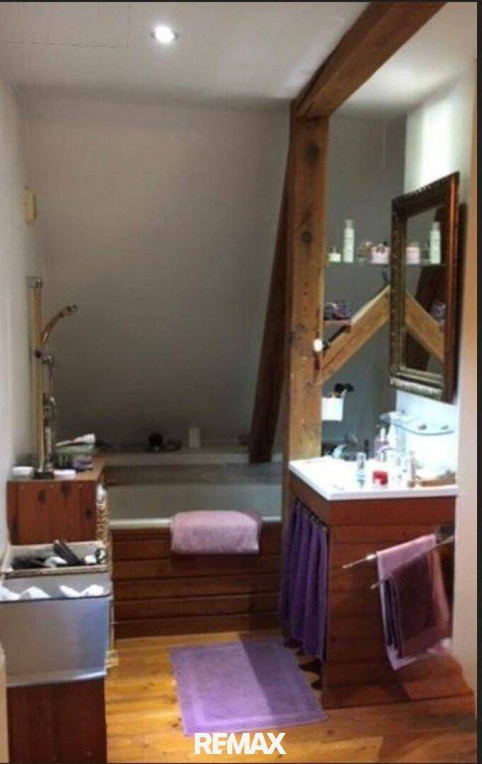 Rustikales Badezimmer mit Holzbalken, Dachschräge und Badewanne, gemütlich und funktional.