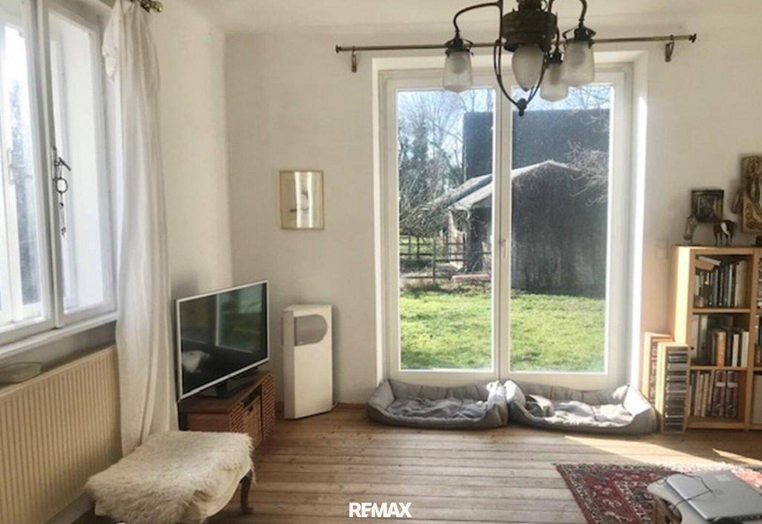 Helles Wohnzimmer mit Holzboden, großem Fenster und Blick ins Grüne, gemütlich eingerichtet.