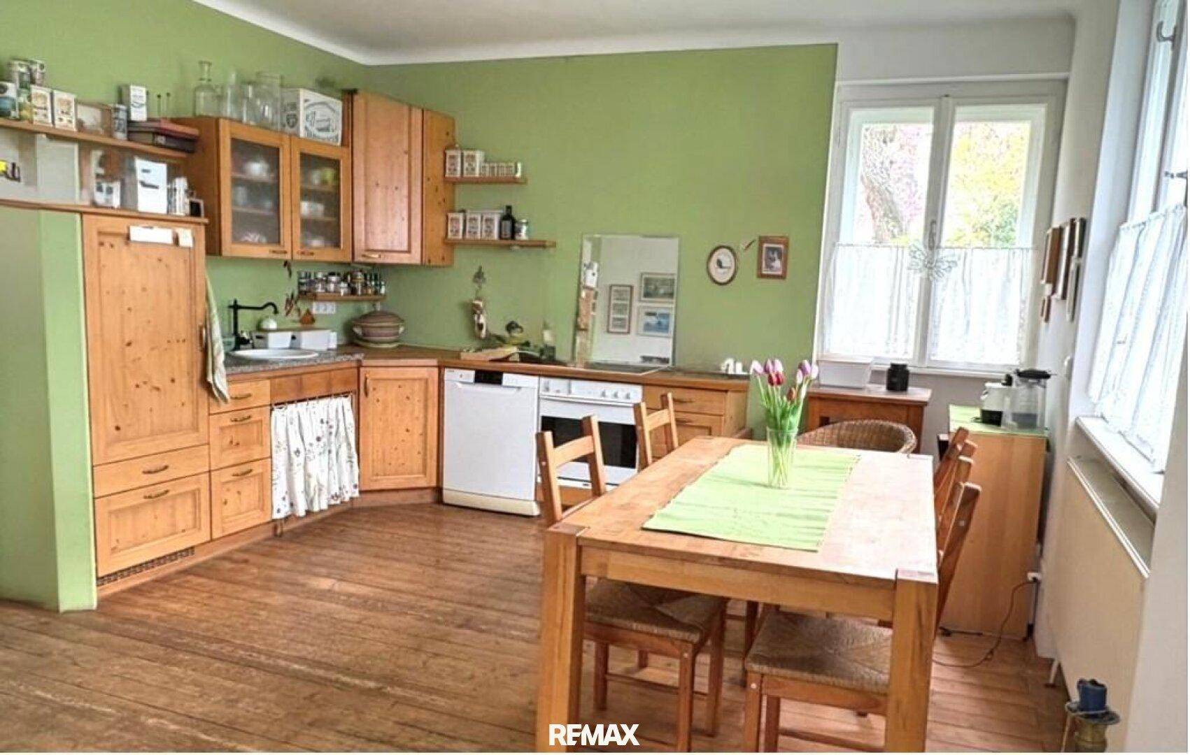 Gemütliche Küche mit Holzschränken, grünen Wänden und einem Esstisch, ideal für Familienmahlzeiten.