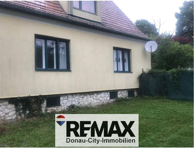Rückseite des Hauses mit gelber Fassade, Ziegeldach und grünem Rasen.