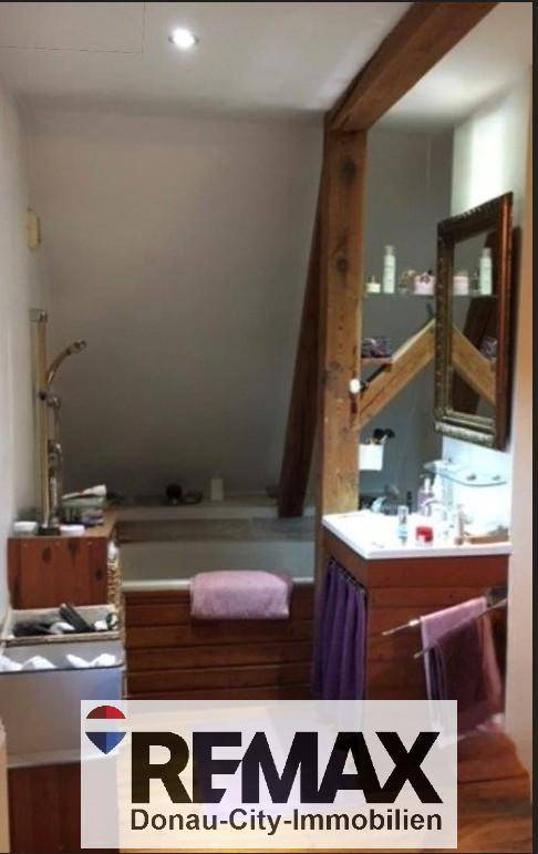 Badezimmer im Dachgeschoss mit Holzbalken, Waschbecken und Badewanne.
