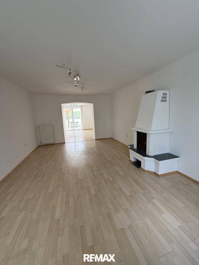 Helles Wohnzimmer mit Parkettboden, Kamin und Zugang zu einem weiteren Raum.
