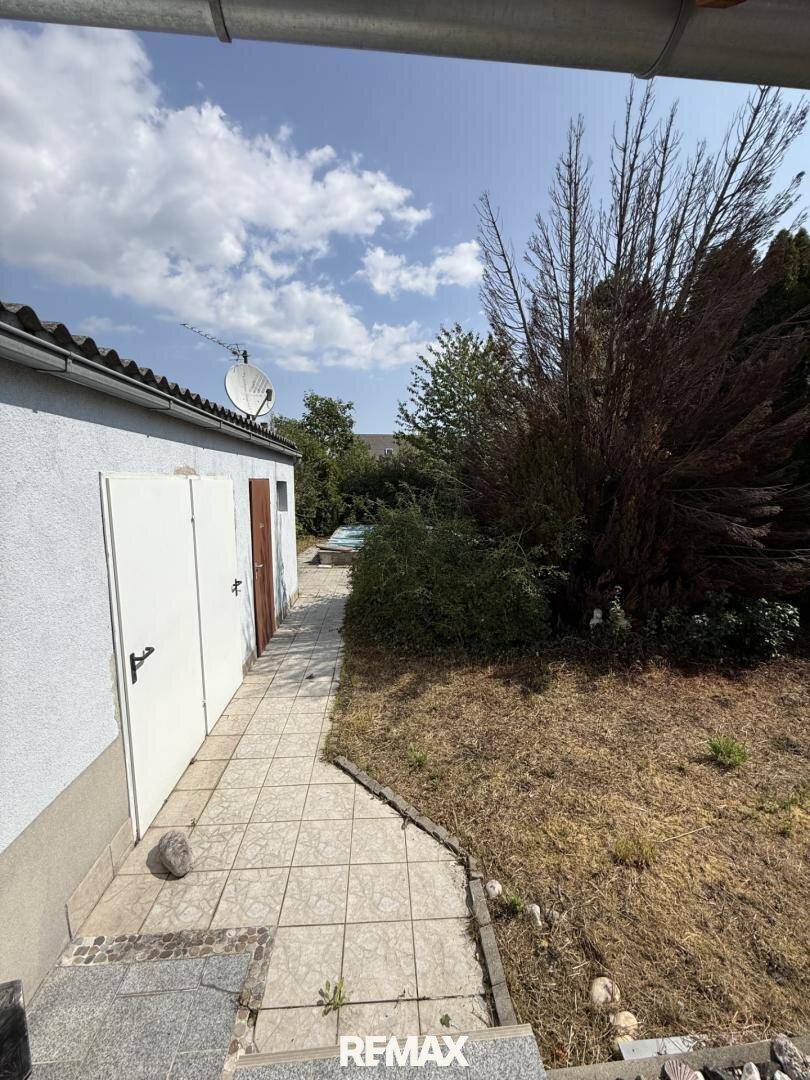 Gartenweg entlang des Nebengebäudes mit Blick auf den Garten und den Poolbereich.