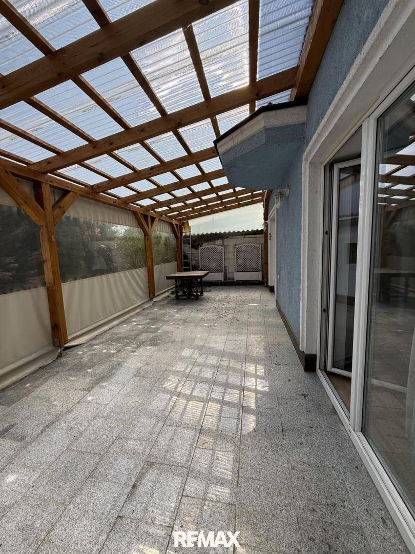 Überdachte Terrasse mit Granitfliesen und Holzbalkenkonstruktion für entspannte Stunden im Freien.