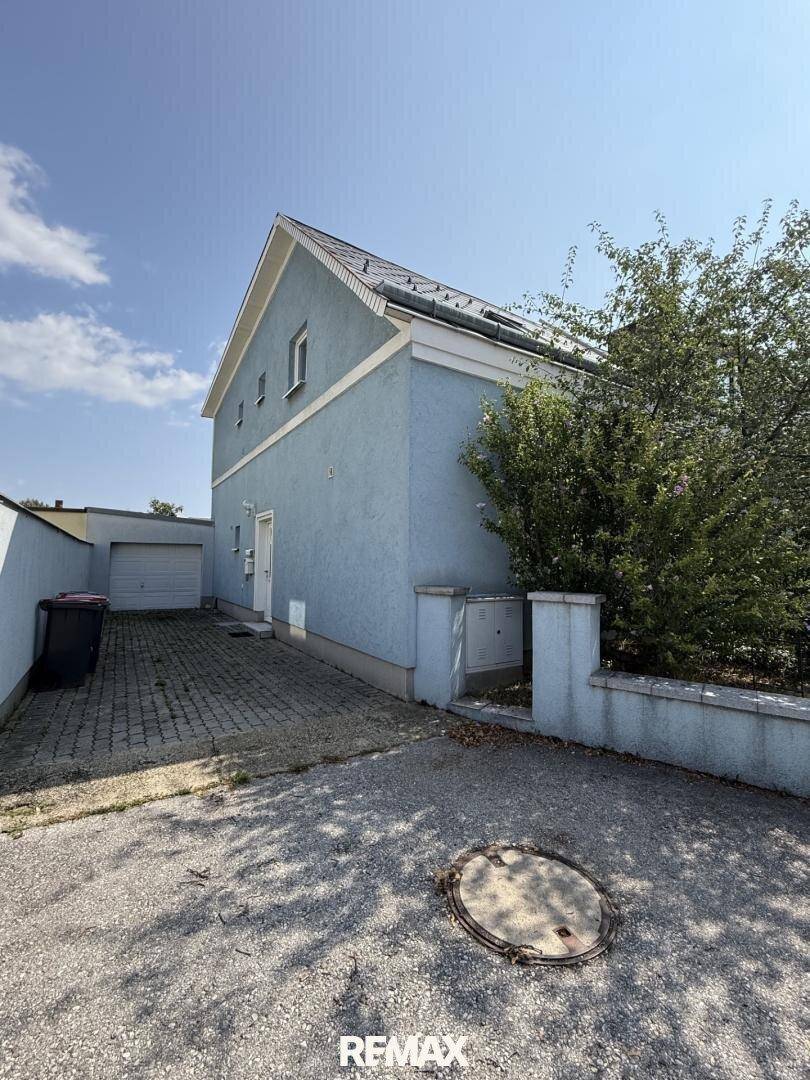 Seitenansicht des Hauses mit Satteldach, Kiesfläche und Garagengebäude.