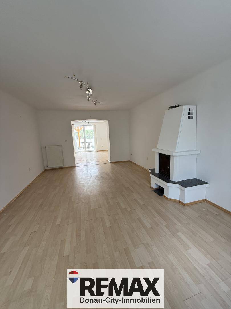 Großes Wohnzimmer mit hellem Holzfußboden und einem gemütlichen Kamin als Mittelpunkt.