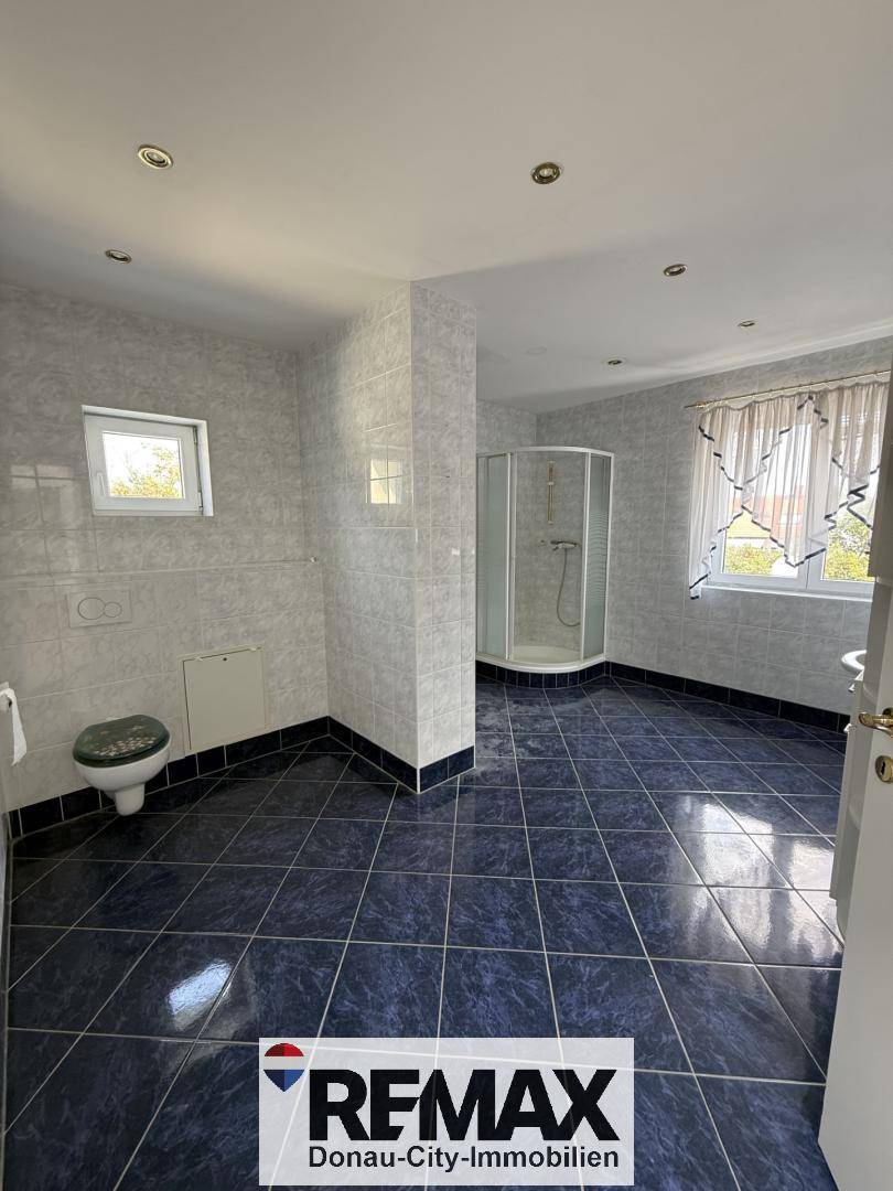 Geräumiges Badezimmer mit dunklen Fliesen, Dusche, Toilette und einem Fenster für Tageslicht.