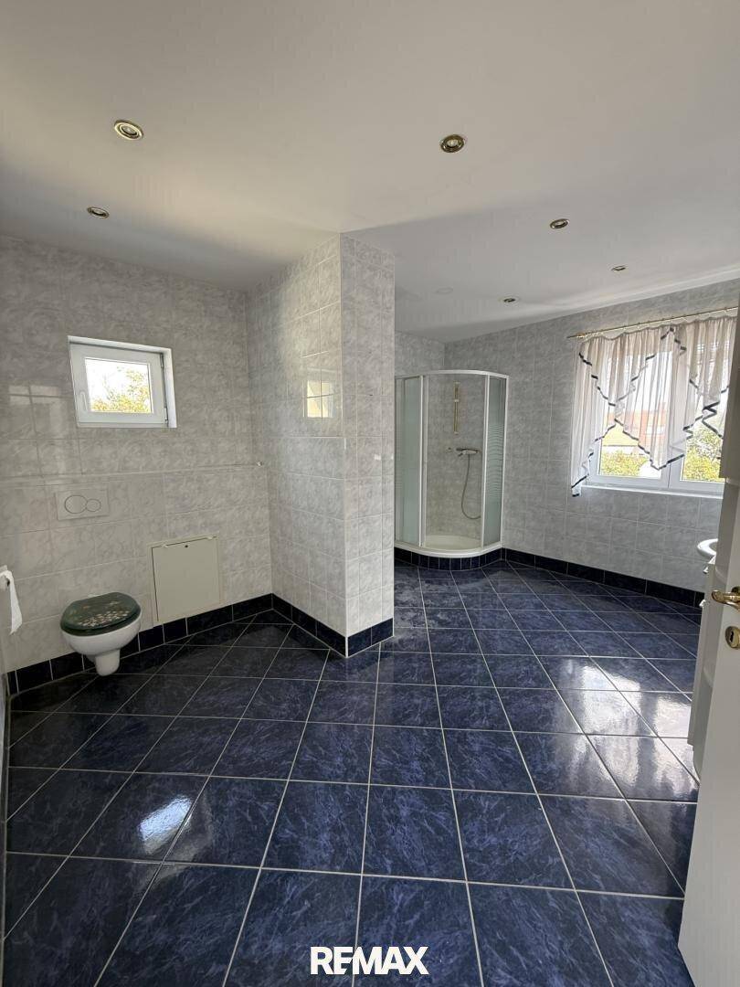 Geräumiges Badezimmer mit blauen Fliesen, Duschkabine und Fenster für Tageslicht.
