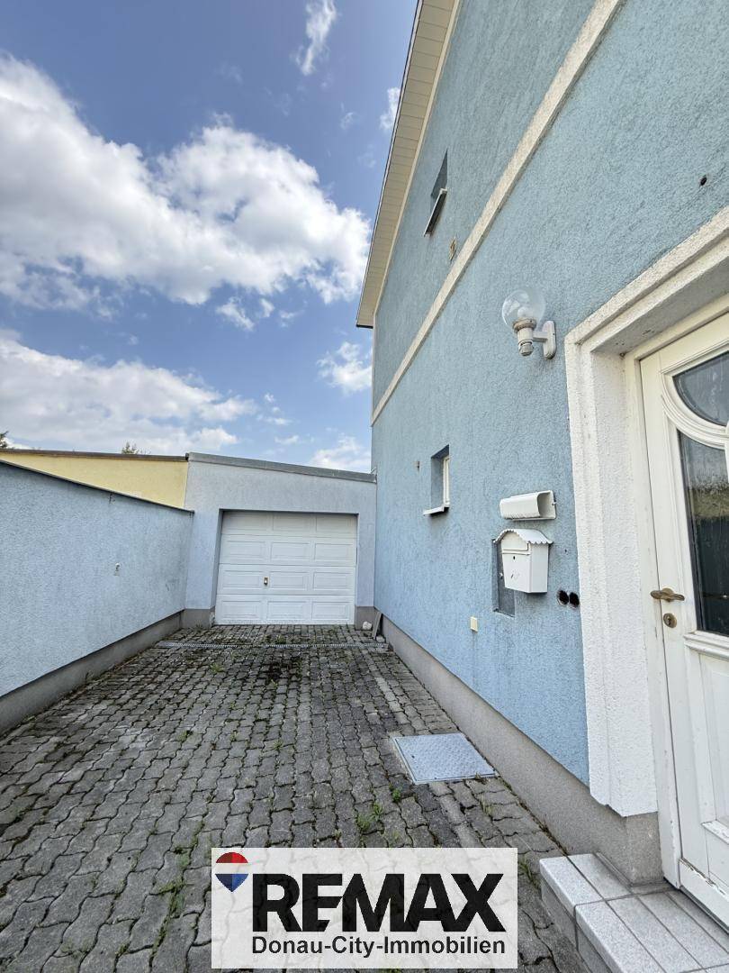 Seitenansicht des Hauses mit gepflasterter Einfahrt, einer Garage und dem Eingangsbereich.