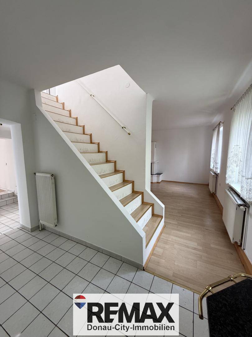 Heller Eingangsbereich mit Treppe zum Obergeschoss und einer Kombination aus Fliesen- und Holzfußboden.