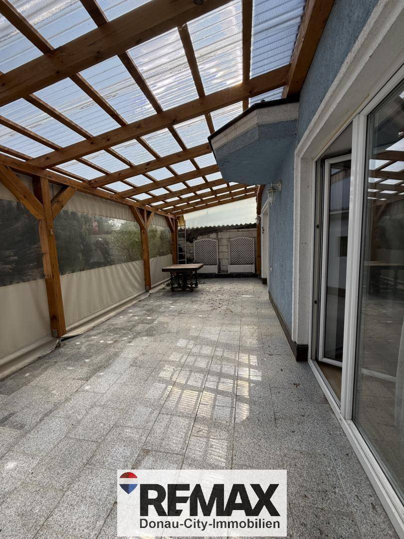 Überdachte Terrasse mit Holzbalkenkonstruktion und Fliesenboden, ideal für Mahlzeiten im Freien.