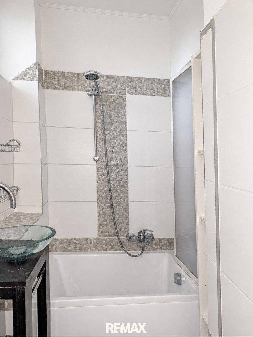 Badezimmer mit Badewanne, Duschfunktion und modernem Glaswaschbecken.