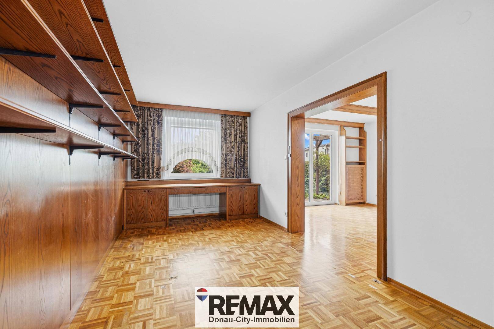 Gemütliches Arbeitszimmer mit Holzvertäfelung, Einbauregalen und Blick ins Grüne.
