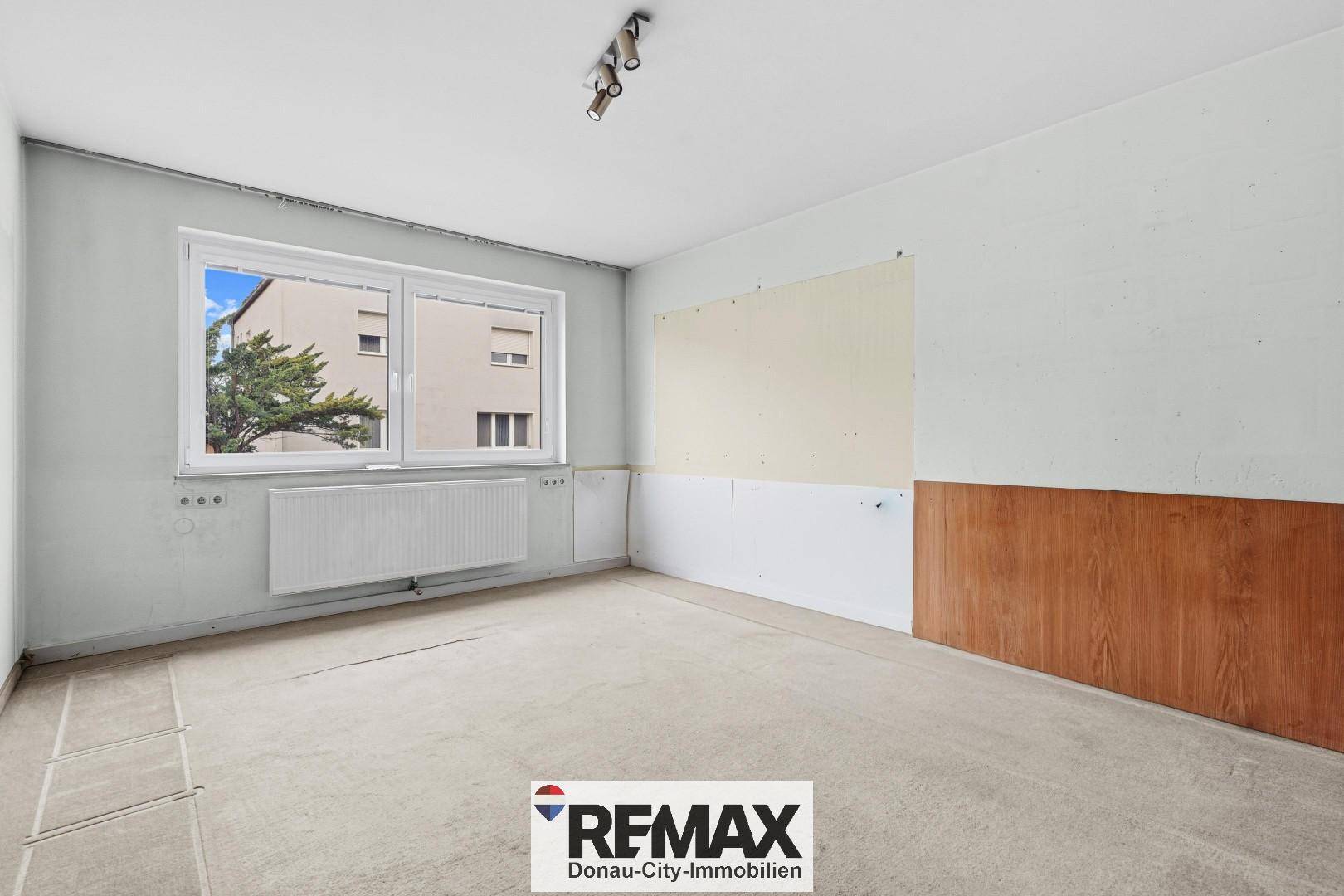 Geräumiges Schlafzimmer mit großem Fenster, Heizkörper und vorbereitetem Bodenbelag.