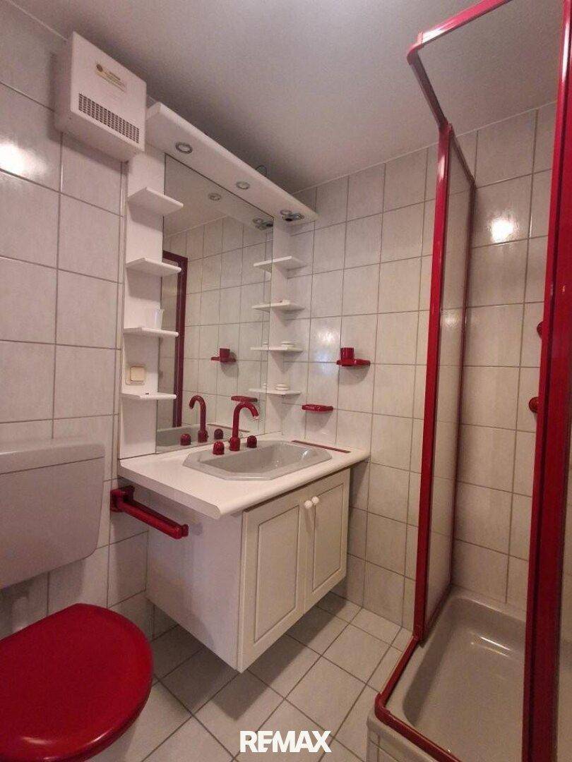 Badezimmer mit roter Duschkabine, Waschbecken und weißen Fliesen.