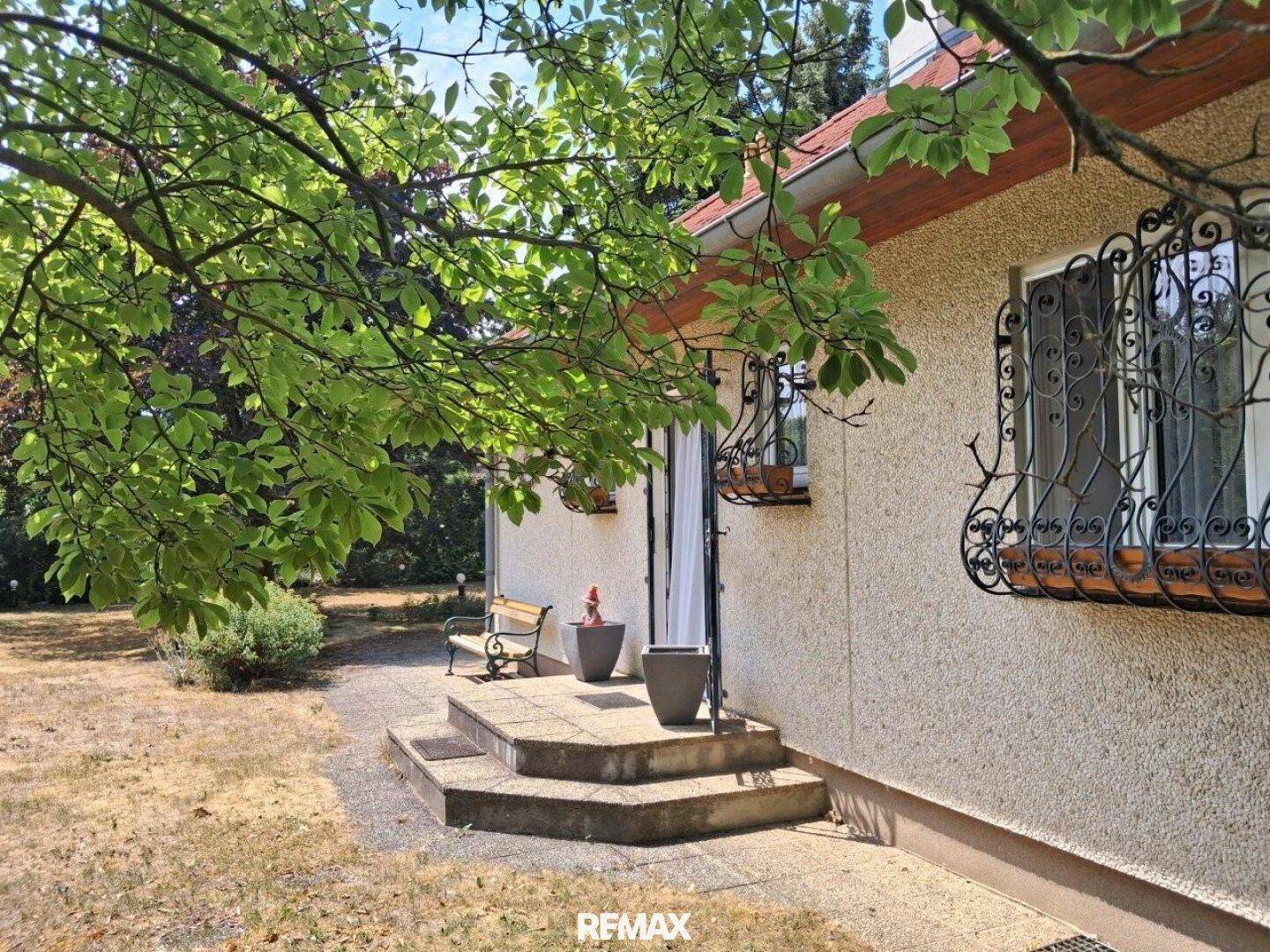 Eingangsbereich des Hauses mit Steinstufen, einer Bank und dekorativen Fenstergittern.