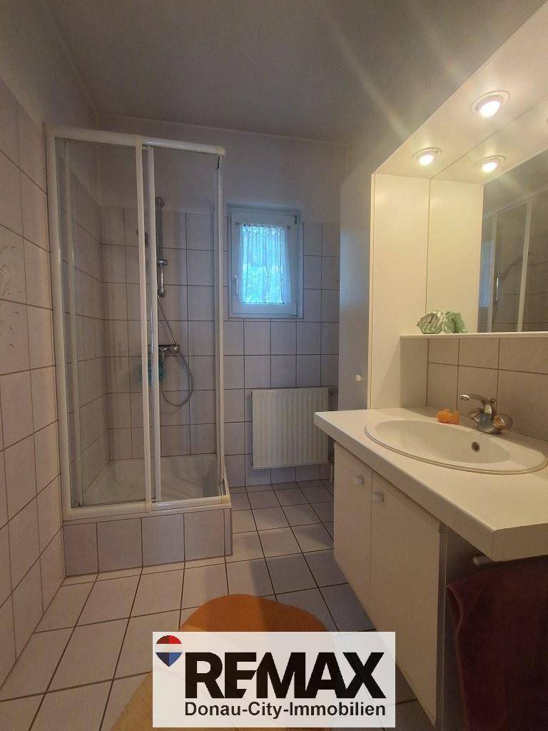 Badezimmer mit Duschkabine, Waschbecken und Fliesen an Wänden und Boden.
