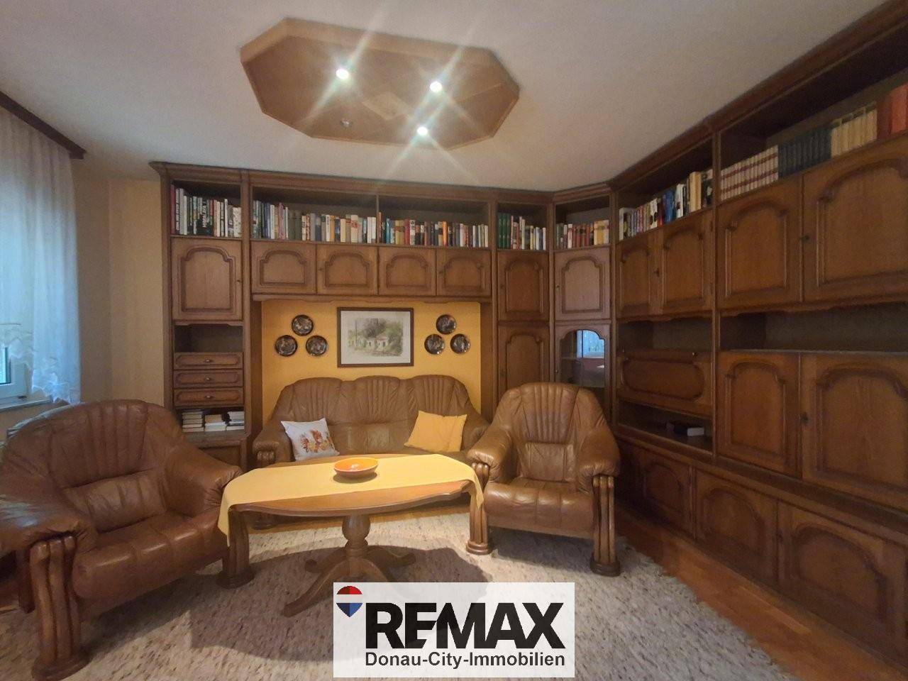 Wohnzimmer mit großer Holzschrankwand, Ledersofas und Teppichboden.
