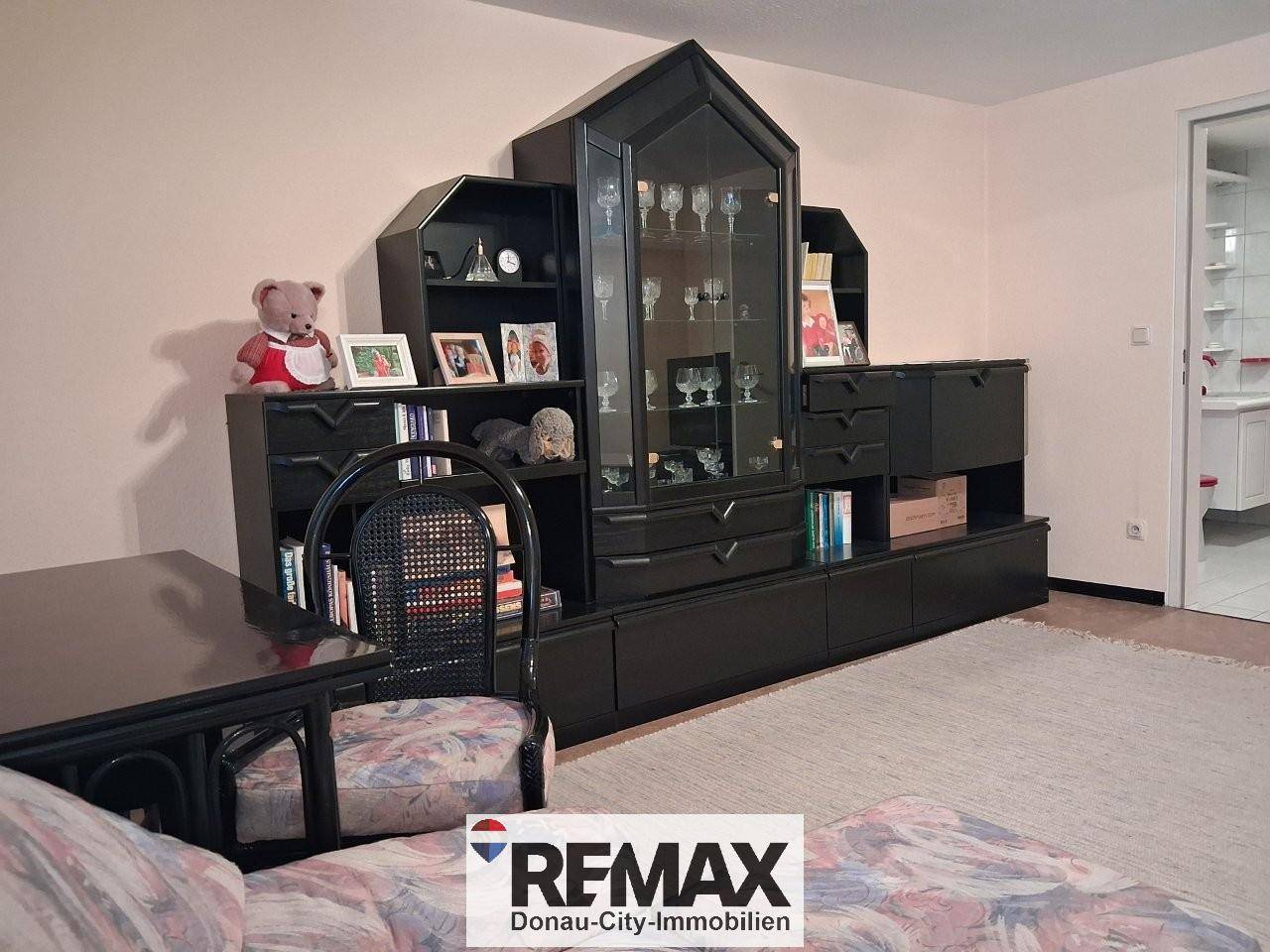 Wohnbereich mit dunkler Vitrine, Sofa und Blick auf einen angrenzenden Raum.