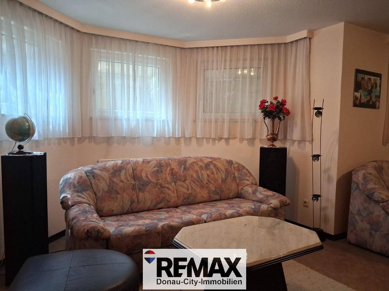 Geräumiges Wohnzimmer mit gemustertem Sofa, Couchtisch und großen Fenstern.