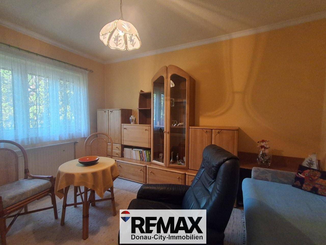 Wohnzimmer mit Holzmöbeln, gelben Wänden und einem Fenster mit Gardinen.