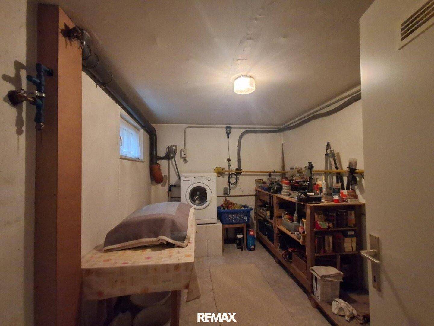 Kellerraum mit Waschmaschine, Regalen und sichtbaren Installationen, ideal als Waschküche.