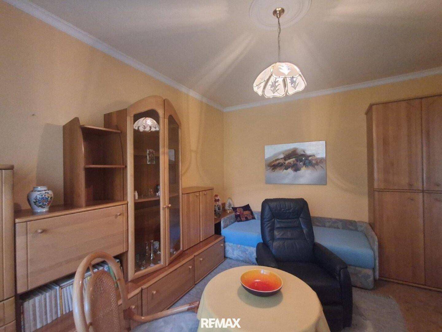 Zimmer mit Holzmöbeln, Sofa und einem Fenster mit Vorhängen.