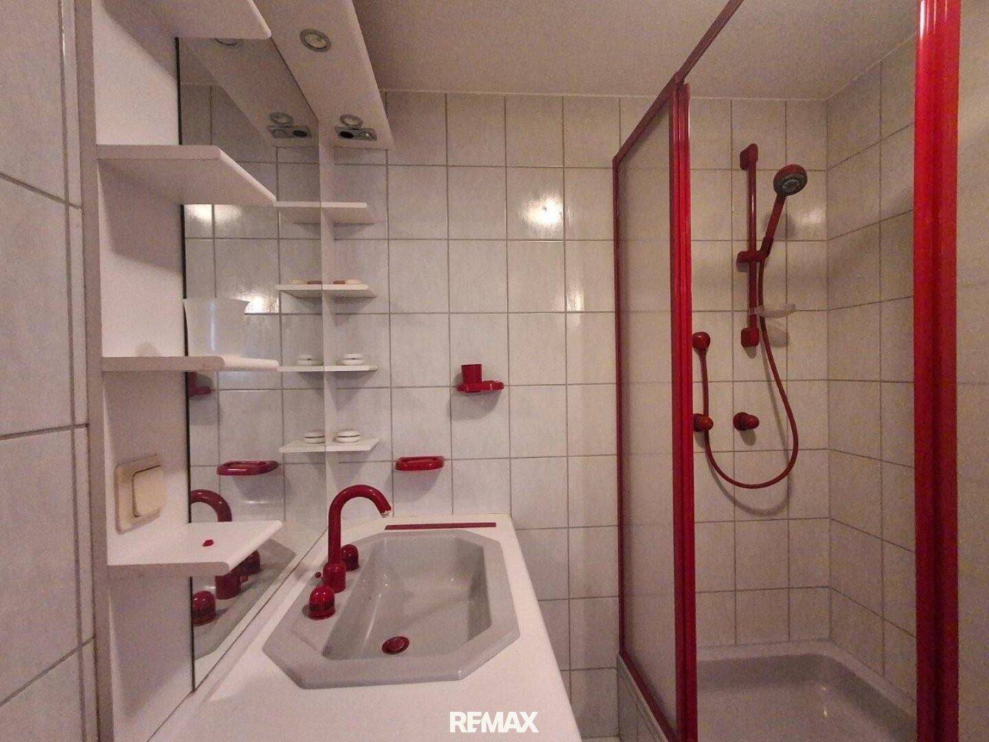 Badezimmer mit roter Duschkabine, Waschbecken und weißen Fliesen.
