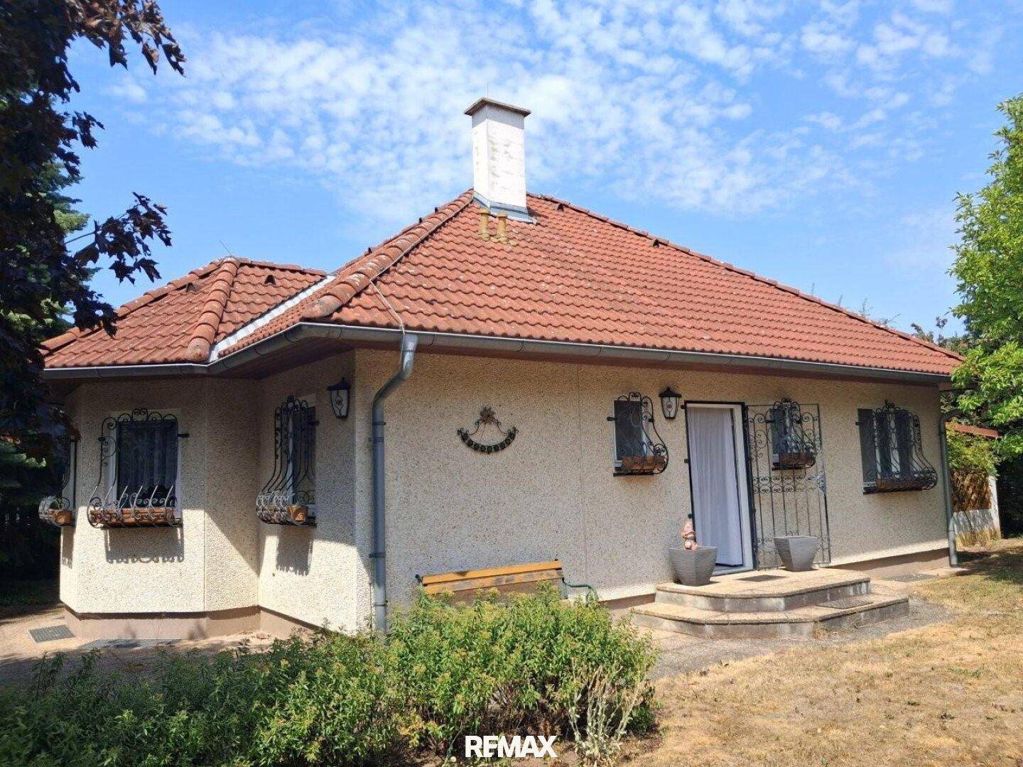 Freistehendes Haus mit rotem Ziegeldach und gepflegtem Garten unter blauem Himmel.