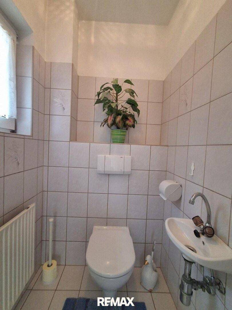 Separate Toilette mit Waschbecken, Fenster und weißen Fliesen.