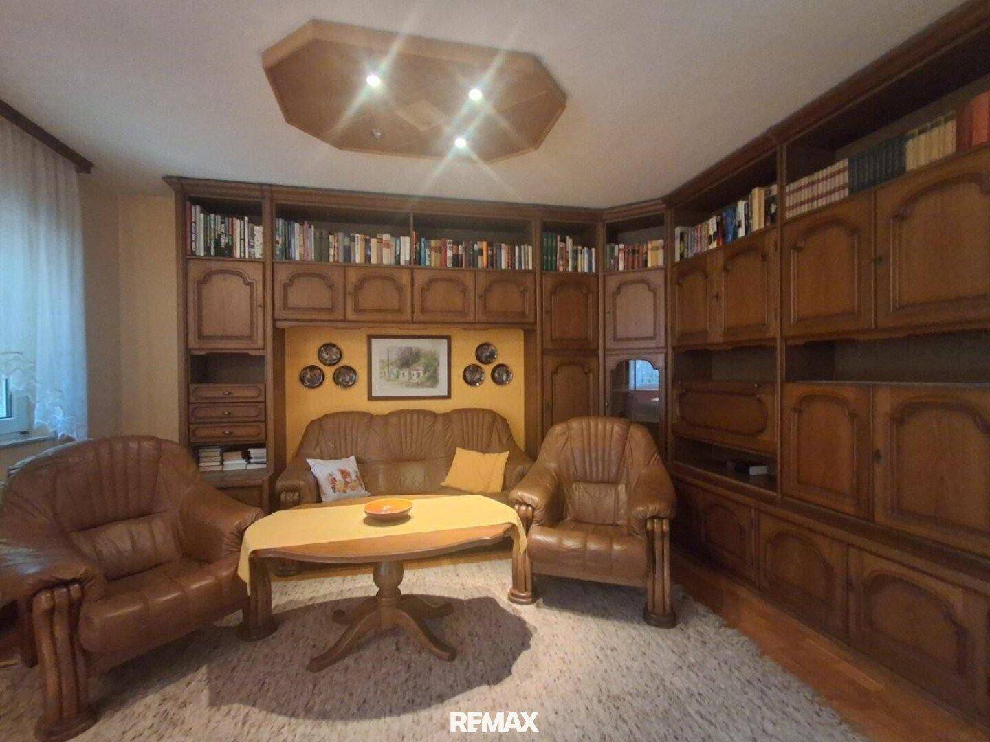Geräumiges Wohnzimmer mit großer Bücherwand aus Holz und bequemen Ledersofas.