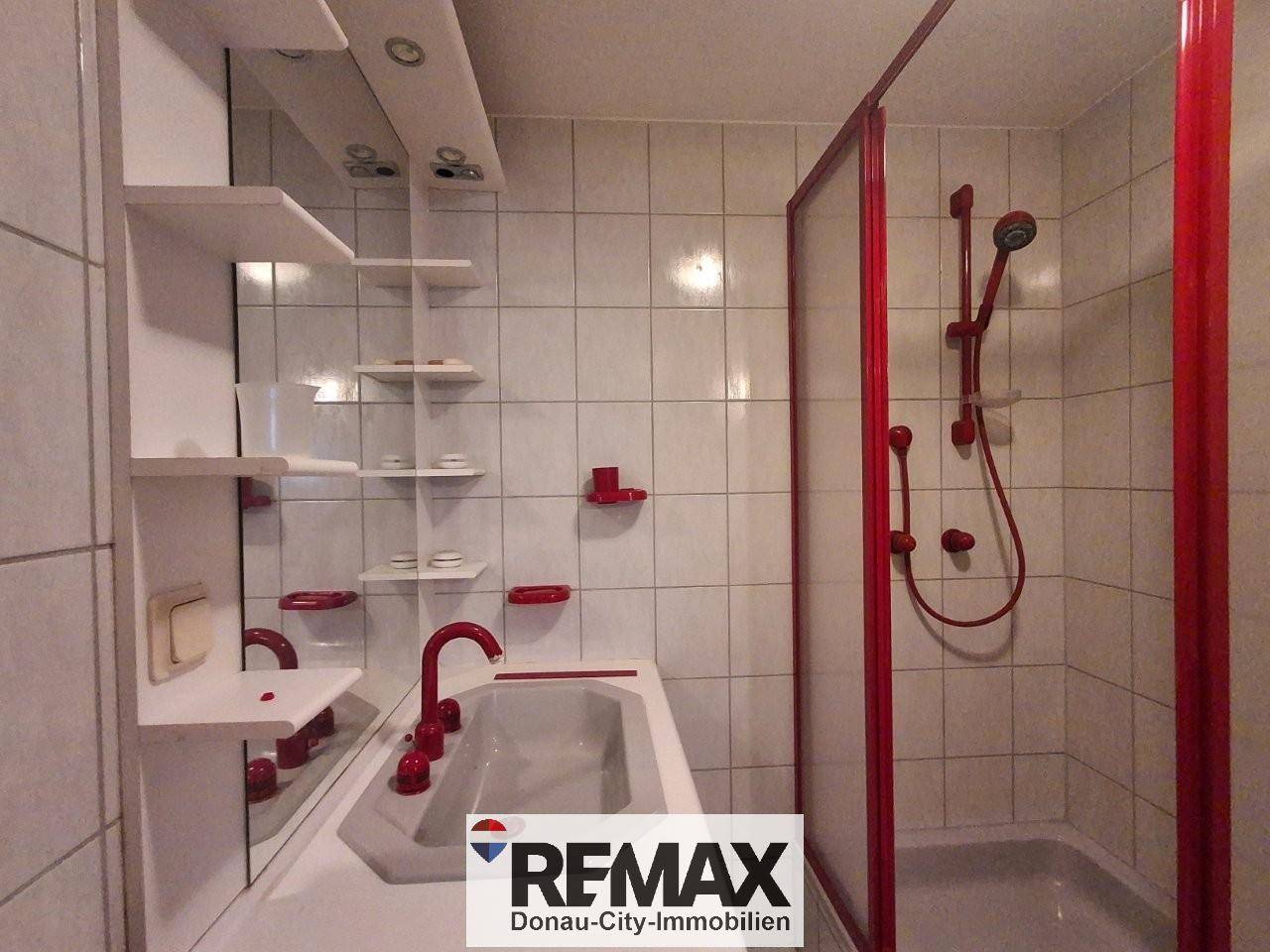 Badezimmer mit Duschkabine, Waschbecken und roten Akzenten.