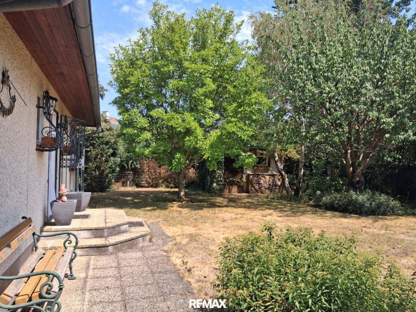 Blick vom Hauseingang in den Garten mit Sitzbank und altem Baumbestand.
