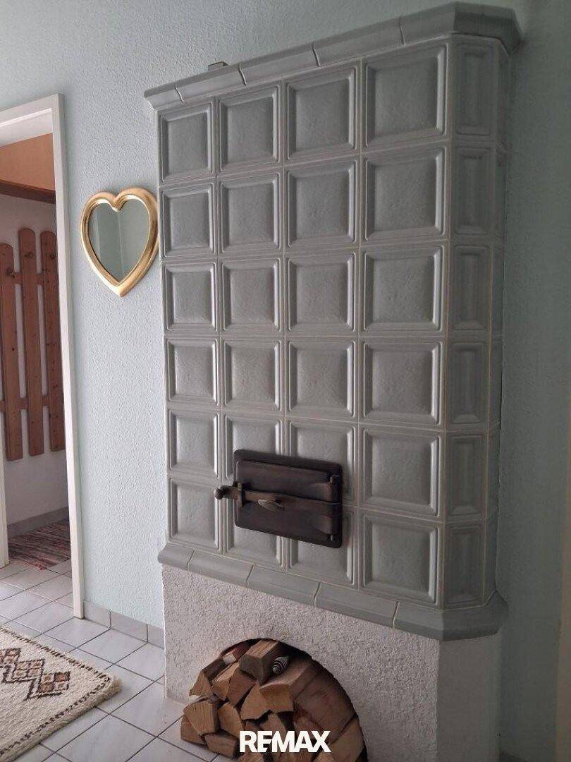 Detailansicht eines traditionellen Kachelofens mit Holzscheiten im Flur.