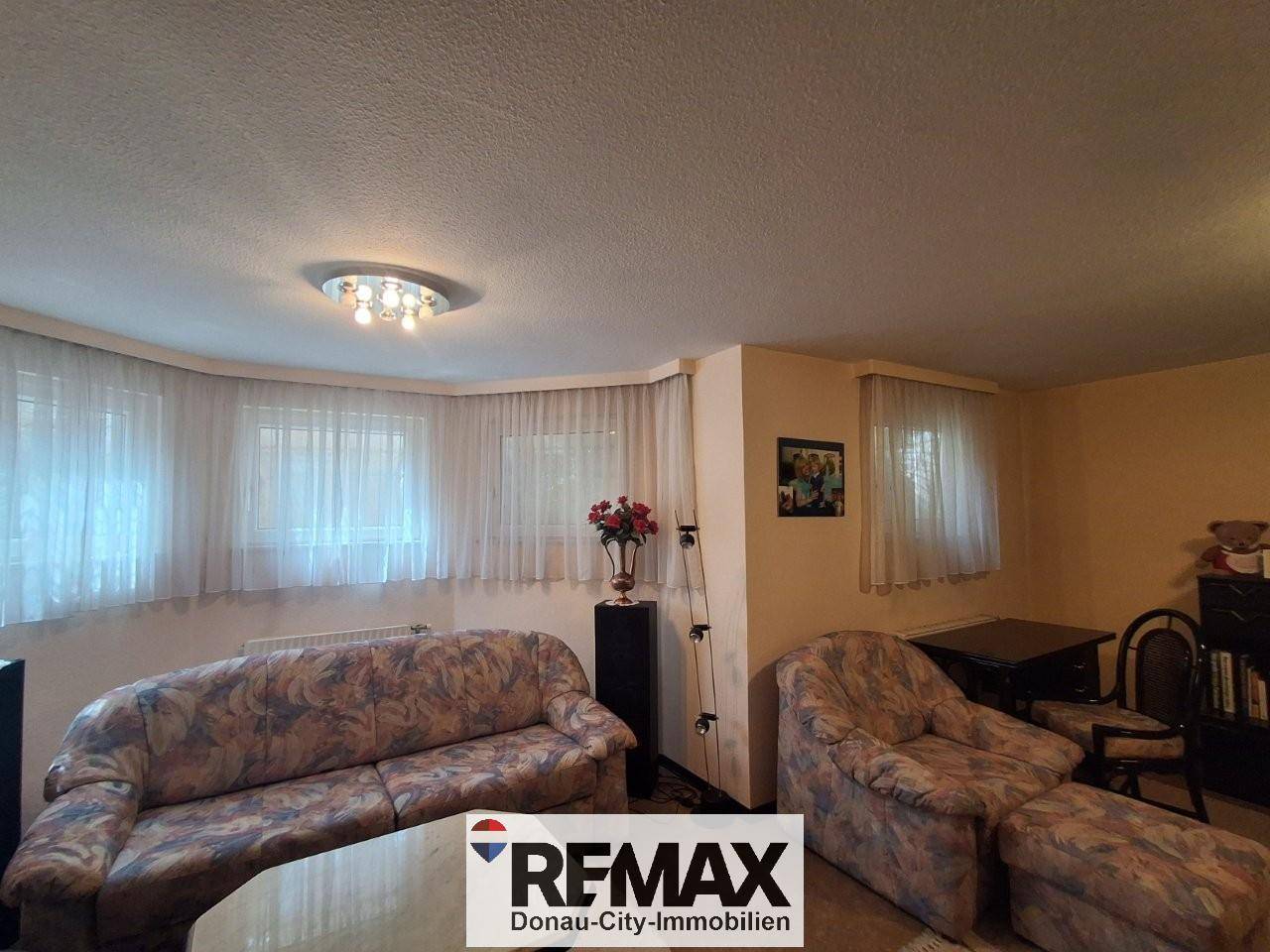 Gemütliches Wohnzimmer mit beigen Sofas, Vorhängen und einem kleinen Couchtisch.