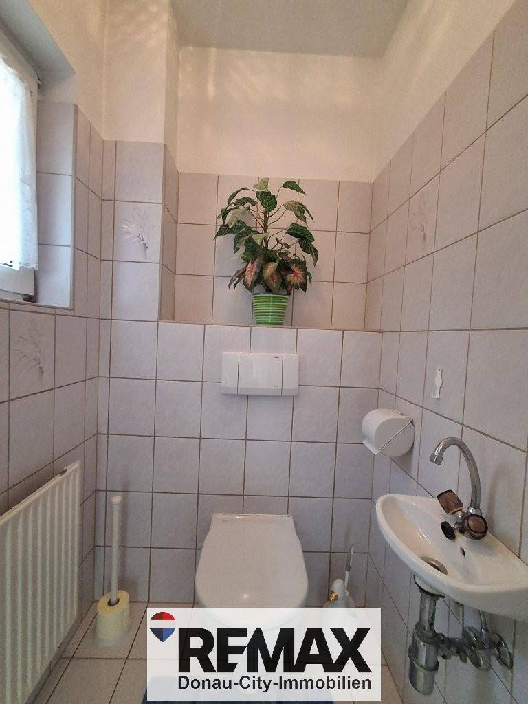 Separate Toilette mit Waschbecken, Fenster und Fliesen an Wänden und Boden.