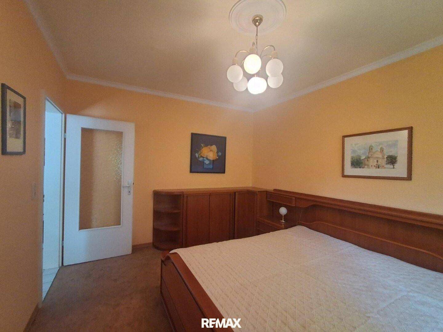 Schlafzimmer mit Doppelbett, Holzmöbeln und einem Fenster mit Vorhängen.
