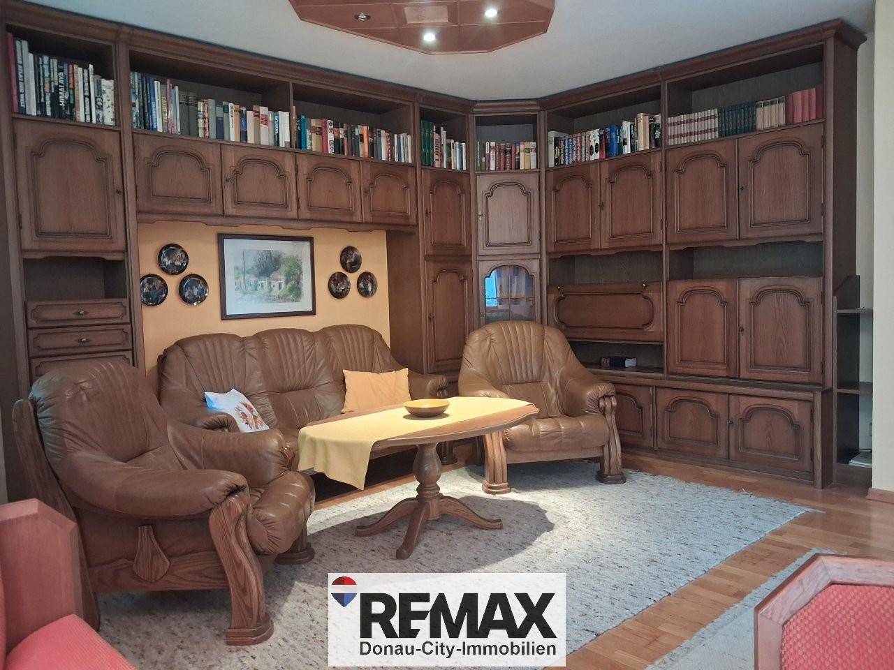 Gemütliches Wohnzimmer mit großer Holzschrankwand, Ledersofas und Teppichboden.