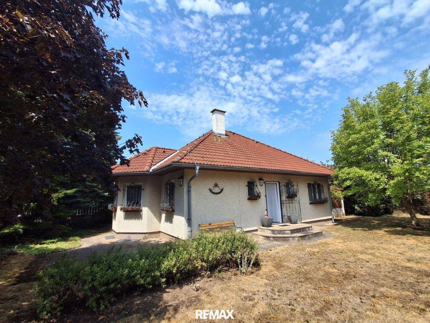 Ansicht des Hauses mit rotem Ziegeldach und großem Garten unter blauem Himmel.